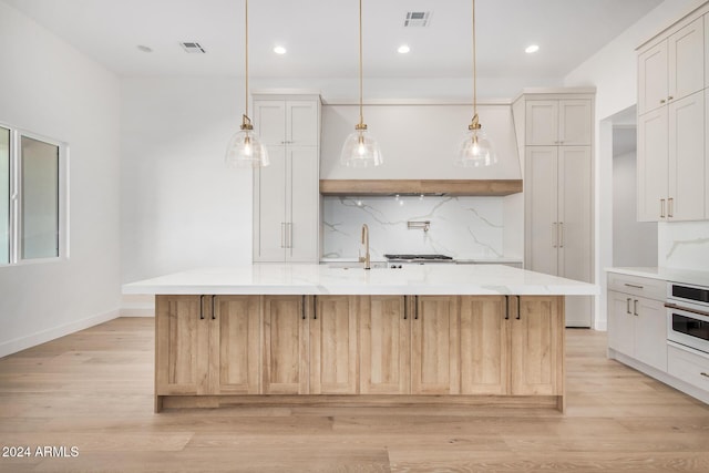 kitchen featuring white oven, a large island with sink, and light hardwood / wood-style flooring