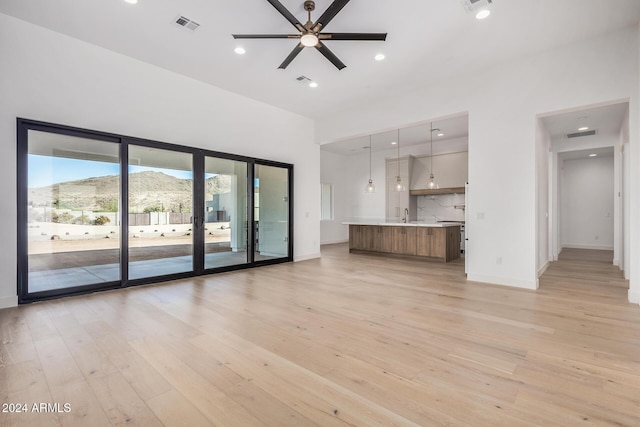 unfurnished living room with a mountain view, ceiling fan, and light hardwood / wood-style flooring