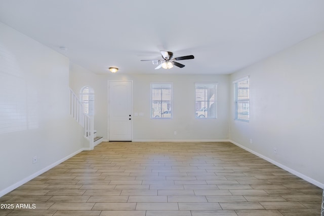 unfurnished room with light wood-type flooring, ceiling fan, baseboards, and stairs