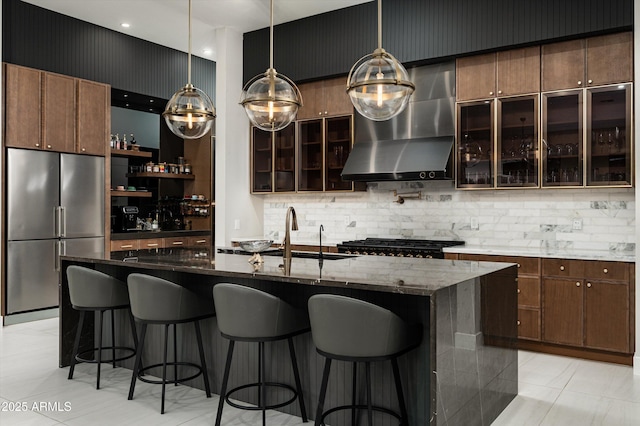 kitchen with dark brown cabinetry, pendant lighting, wall chimney range hood, and stainless steel refrigerator