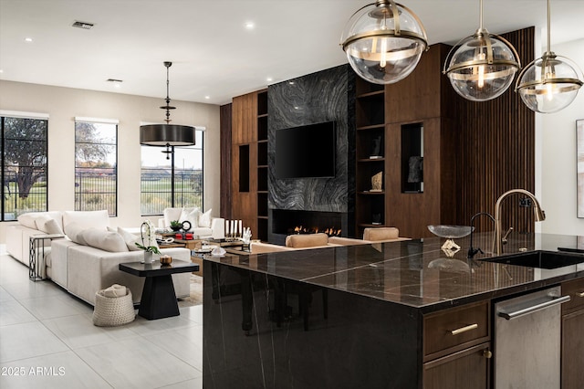 kitchen with sink, a premium fireplace, dark brown cabinetry, a center island with sink, and dark stone counters