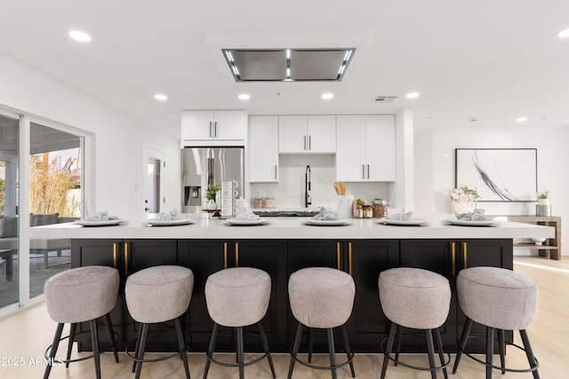 kitchen with a kitchen breakfast bar, stainless steel fridge, a large island with sink, and white cabinets