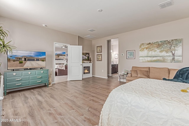 9429 E Grapefruit Dr, Florence, AZ 85132 - bedroom featuring light wood-type flooring, a glass covered fireplace, ensuite bath, and baseboards