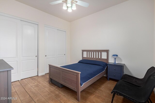 bedroom with ceiling fan, light hardwood / wood-style flooring, and multiple closets