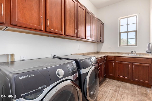 clothes washing area with light wood-type flooring, sink, washing machine and clothes dryer, and cabinets