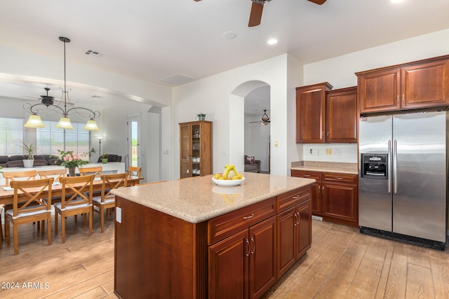 kitchen with pendant lighting, light wood-type flooring, stainless steel refrigerator with ice dispenser, a center island, and ceiling fan with notable chandelier