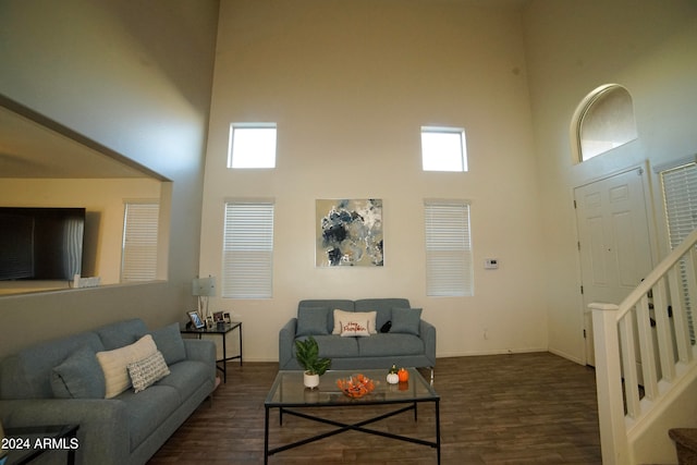 living room with a towering ceiling and dark wood-type flooring