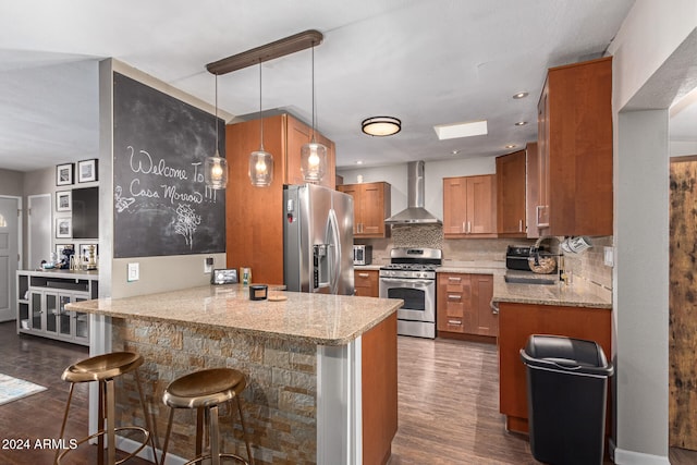 kitchen with wall chimney range hood, kitchen peninsula, stainless steel appliances, pendant lighting, and a breakfast bar