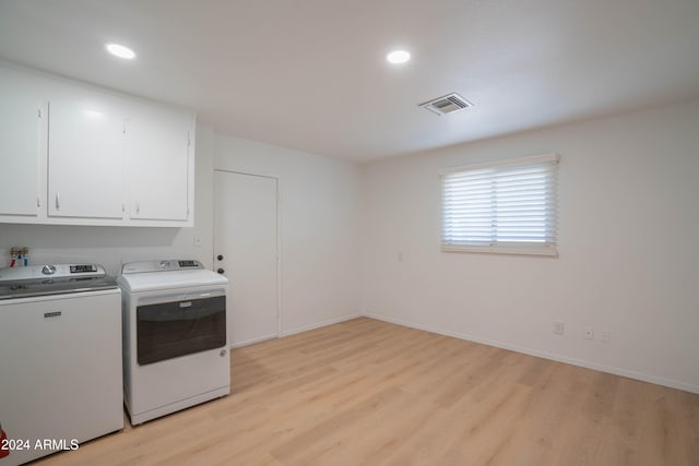 washroom featuring cabinets, washing machine and dryer, and light hardwood / wood-style flooring