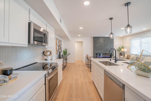 kitchen with light hardwood / wood-style floors, white cabinetry, sink, appliances with stainless steel finishes, and decorative light fixtures