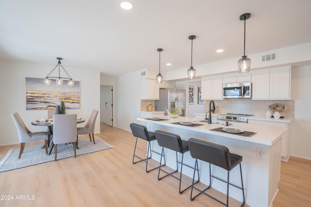 kitchen with light wood-type flooring, white cabinetry, hanging light fixtures, and stainless steel appliances