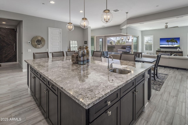 kitchen featuring sink, light hardwood / wood-style flooring, an island with sink, decorative light fixtures, and light stone counters