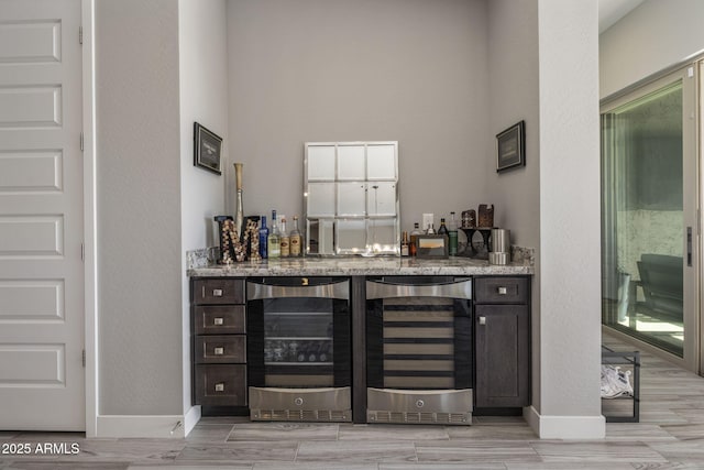 bar with wine cooler, light stone countertops, and dark brown cabinetry