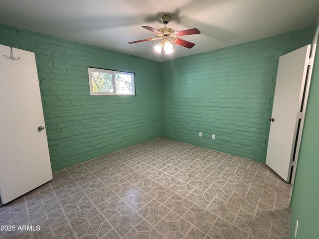 unfurnished room with tile patterned floors, ceiling fan, and brick wall