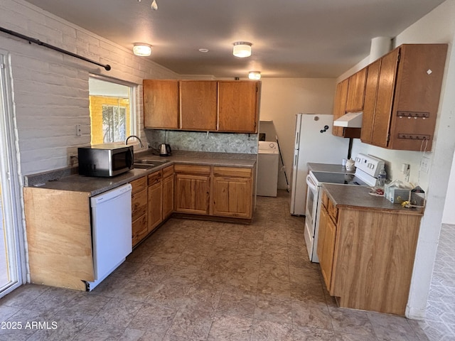 kitchen with brown cabinets, a sink, washer / clothes dryer, dark countertops, and white appliances