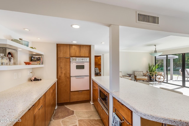 kitchen featuring stainless steel microwave, double oven, and light stone counters