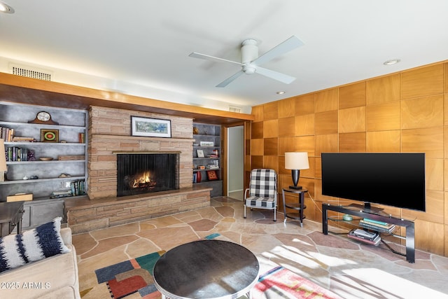 living room with ceiling fan, built in shelves, and a stone fireplace