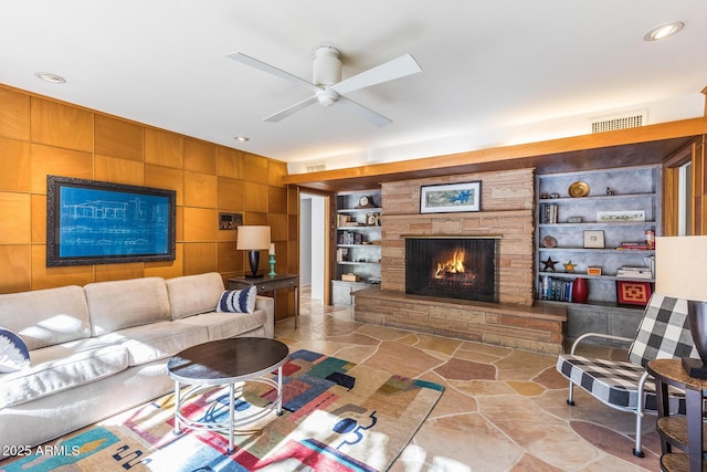 living room with built in features, ceiling fan, and a stone fireplace