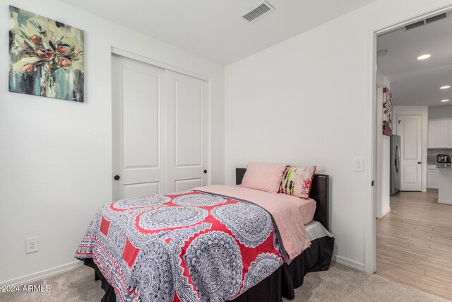 bedroom with light carpet, stainless steel refrigerator, and a closet