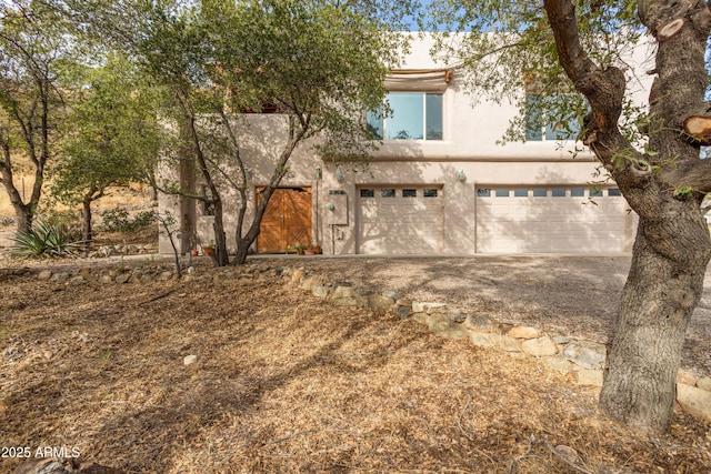 view of front of property featuring a garage, gravel driveway, and stucco siding