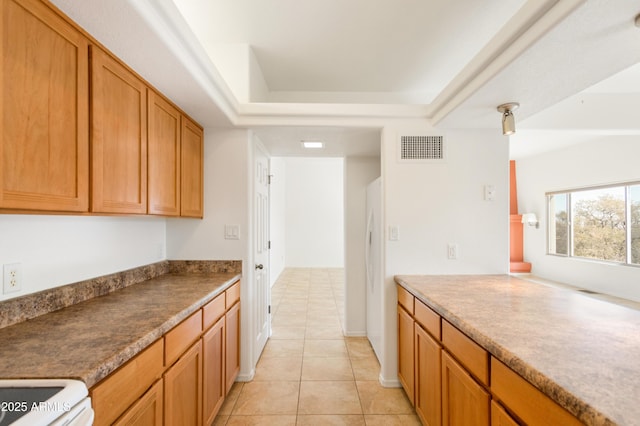 kitchen with light tile patterned floors, visible vents, freestanding refrigerator, brown cabinets, and a tray ceiling