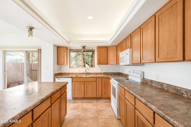 kitchen featuring white appliances, light tile patterned floors, dark countertops, a tray ceiling, and a sink