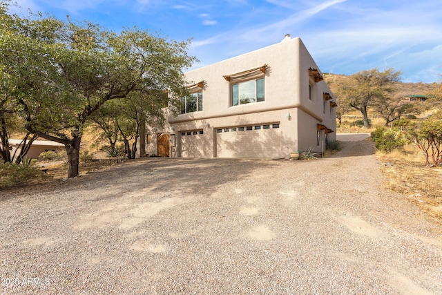 view of front of house with a garage, gravel driveway, and stucco siding