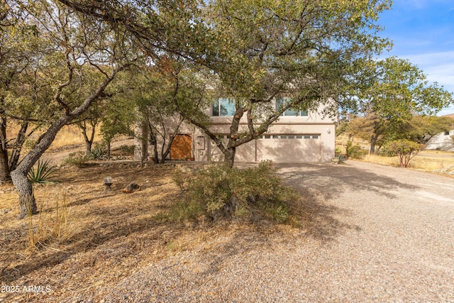 view of front of property featuring an attached garage, dirt driveway, and stucco siding