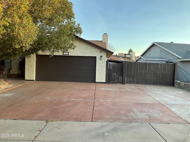 ranch-style house featuring a chimney, stucco siding, concrete driveway, an attached garage, and a gate