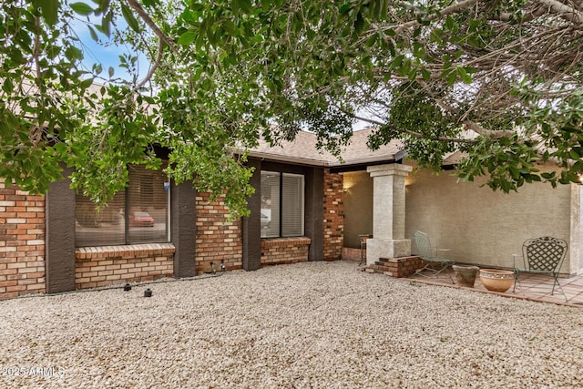 entrance to property with brick siding, a patio area, and roof with shingles