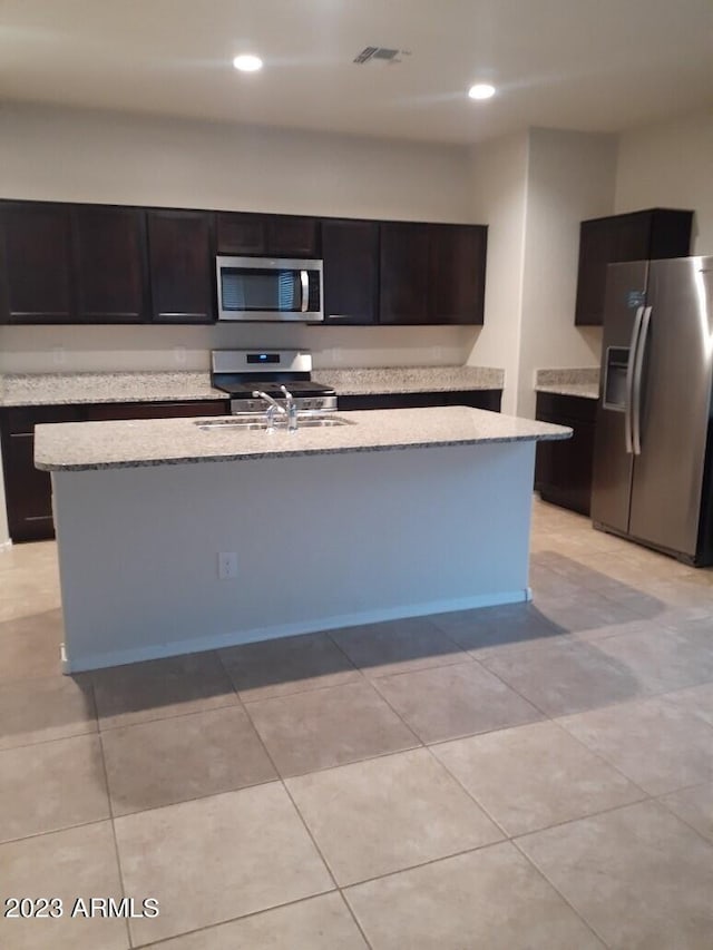 kitchen featuring a center island with sink, appliances with stainless steel finishes, light tile floors, and light stone counters