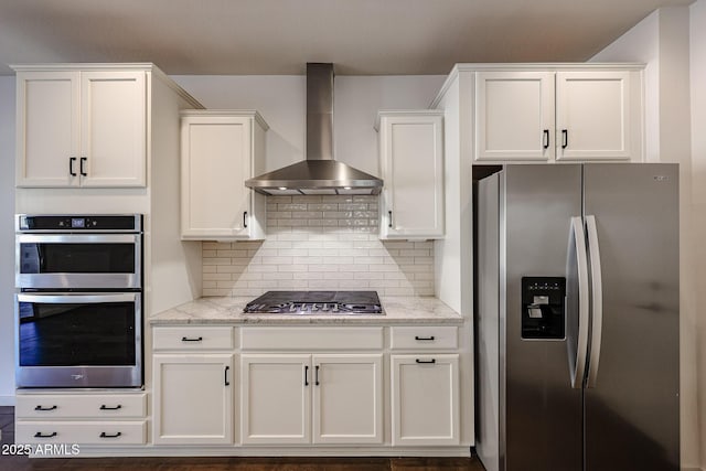 kitchen with white cabinets, appliances with stainless steel finishes, light stone countertops, and wall chimney range hood