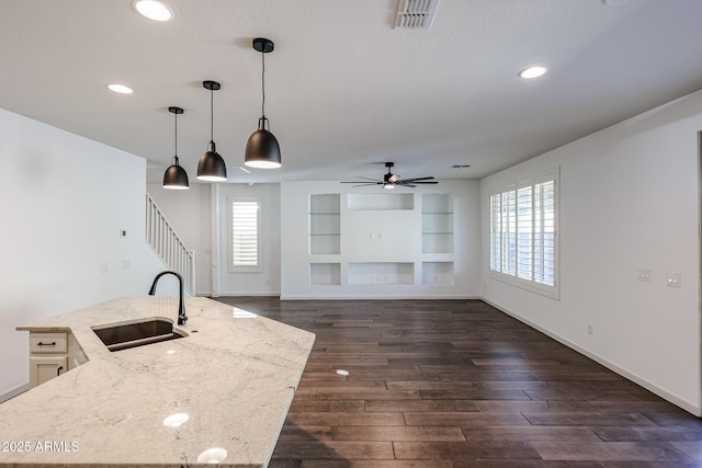 kitchen with sink, dark hardwood / wood-style floors, hanging light fixtures, and a center island with sink