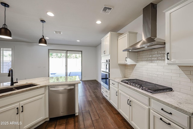 kitchen with appliances with stainless steel finishes, pendant lighting, wall chimney range hood, and light stone counters