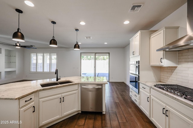 kitchen featuring wall chimney exhaust hood, sink, white cabinetry, light stone counters, and appliances with stainless steel finishes