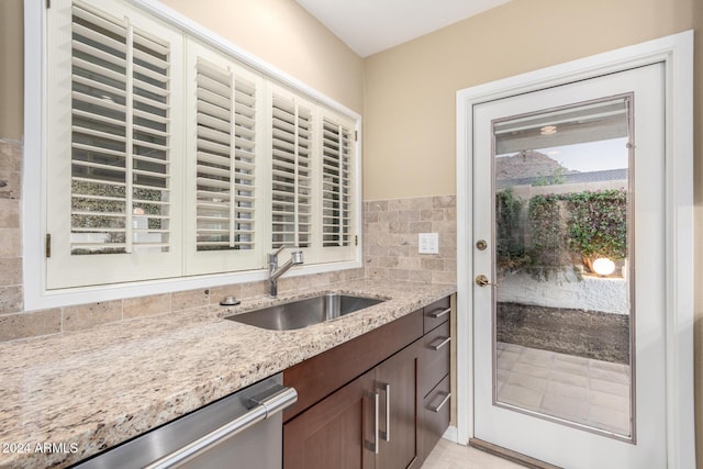 kitchen featuring decorative backsplash, dishwasher, sink, and light stone countertops