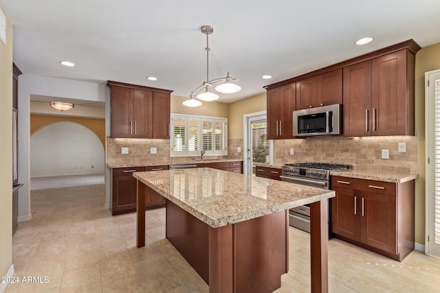 kitchen with light stone countertops, a breakfast bar, stainless steel appliances, decorative light fixtures, and a center island