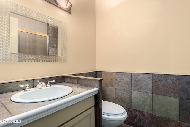 bathroom with vanity, toilet, and tile walls