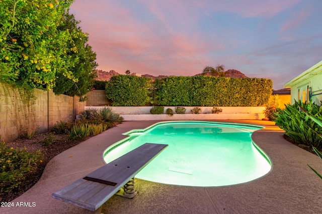 pool at dusk featuring a diving board