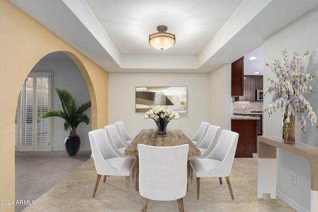 dining area with a raised ceiling and light colored carpet