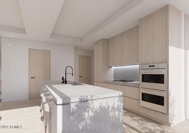 kitchen featuring light hardwood / wood-style floors, a raised ceiling, a center island with sink, double oven, and sink