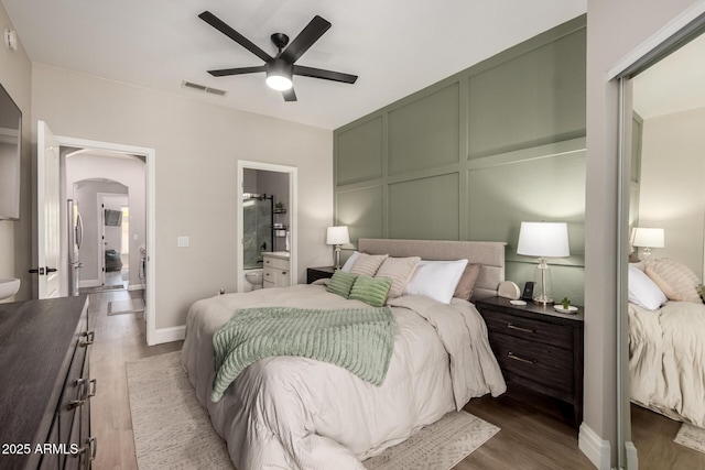 1411 E Orangewood Ave Unit 233, Phoenix, AZ 85020 - bedroom featuring a decorative wall, wood finished floors, arched walkways, a ceiling fan, and connected bathroom