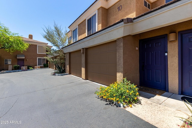 1411 E Orangewood Ave Unit 233, Phoenix, AZ 85020 - view of exterior entry with an attached garage, stucco siding, and asphalt driveway