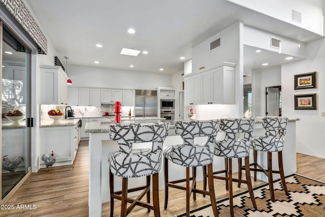 kitchen featuring built in appliances, white cabinets, light stone countertops, and a kitchen bar