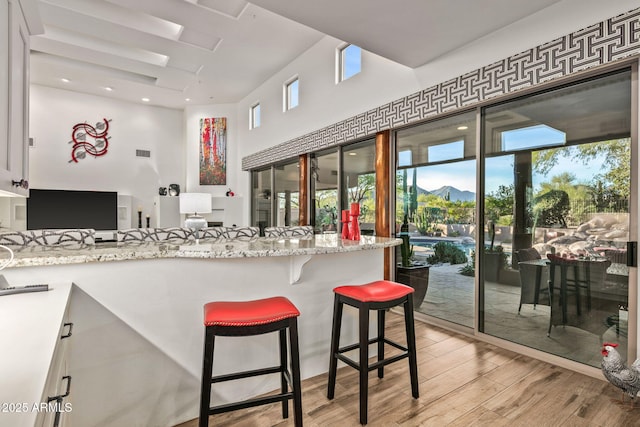 kitchen featuring a mountain view, white cabinetry, a breakfast bar area, and light stone countertops