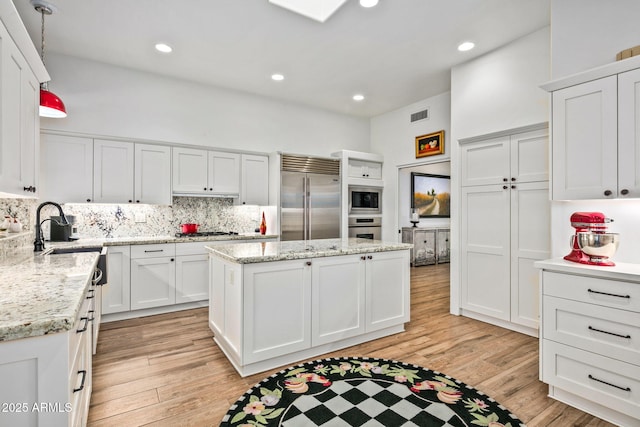 kitchen featuring hanging light fixtures, white cabinets, tasteful backsplash, a kitchen island, and built in appliances