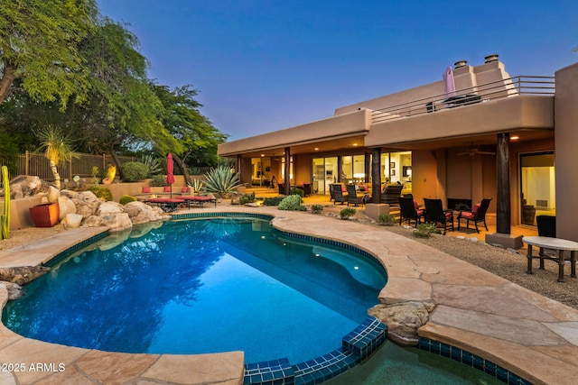 pool at dusk with a patio and ceiling fan