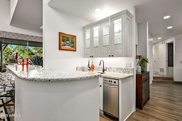 kitchen with hardwood / wood-style floors, light stone countertops, white cabinetry, sink, and a breakfast bar area