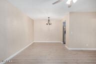 empty room featuring ceiling fan with notable chandelier and light wood-type flooring