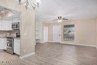 kitchen featuring white cabinets, stainless steel appliances, ceiling fan with notable chandelier, and light wood-type flooring